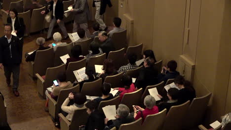 Spectators-sitting-at-a-concert-hall-with-a-program-in-their-hands