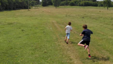 Children-run-and-play-in-green-field---aerial-slow-motion