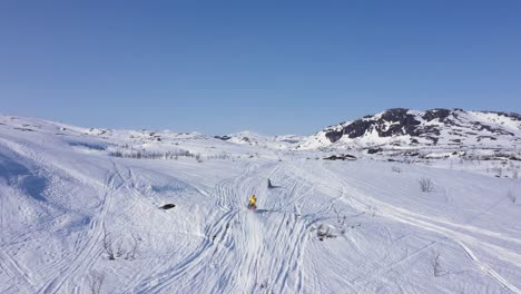 Vista-Aérea-De-Un-Grupo-De-Personas-En-Motos-De-Nieve-En-Un-Paisaje-Montañoso-Nevado