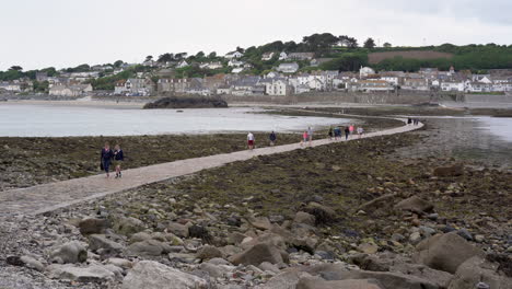 Touristen,-Die-An-Einem-Bewölkten-Frühlingstag-Auf-Dem-Damm-Gehen,-Der-Von-Der-Englischen-Mittelalterlichen-Burg-Und-Der-Kirche-Von-St.-Michael&#39;s-Mount-In-Cornwall-Nach-Marazion-Führt,-4k-aufnahmen