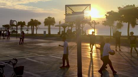 Los-Adolescentes-Juegan-Juegos-De-Baloncesto-En-Las-Canchas-Al-Lado-Del-Océano-Con-El-Resplandor-Del-Sol-En-El-Fondo