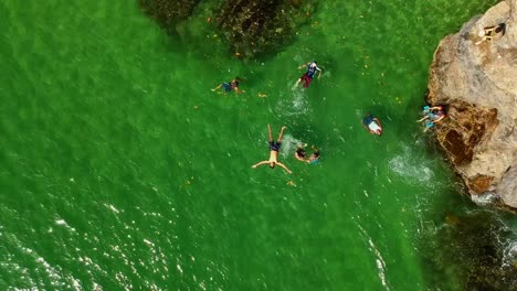 Aerial-rocket-drone-shot-of-a-group-playing-in-a-white-sand-cove-beach