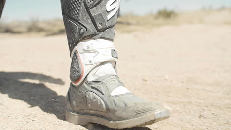 Cámara-Lenta:-Un-Motociclista-Camina-Por-La-Tierra-Y-La-Arena-Del-Desierto-Con-Su-Equipo-Y-Uniforme-De-Motociclista