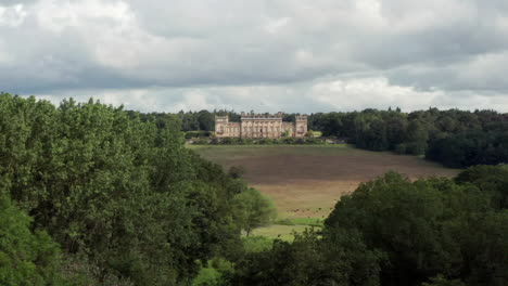 Revelación-Aérea-De-Harewood-House,-Una-Casa-De-Campo-En-West-Yorkshire,-A-Través-De-Las-Copas-De-Los-árboles-Con-Un-Cultivo-Estrecho.