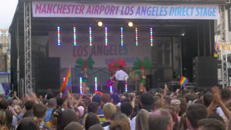 Leeds-Pride-LGBTQ-Festival-2019-shot-of-the-crowd-in-foreground-dancing-and-waving-flags-with-drag-queens-and-salsa-man-on-the-stage-dancing-close-up-focused-on-crowd-with-waving-flags-4K-25P