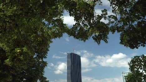 Tilt-down-from-trees-to-Donauinsel-with-UNO-City-in-background,-Vienna