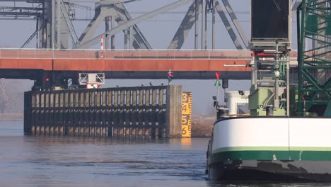 Nahaufnahme-Des-Wasserstraßenkorridors,-Der-Unter-Einer-Brücke-über-Den-Fluss-Ijssel-Im-Hintergrund-Führt,-Mit-Schwerem-Baggerschiff-Im-Vordergrund-Bei-Der-Arbeit