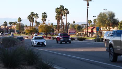 Car-traffic-on-avenue-with-palm-trees-in-La-Quinta,-California,-USA