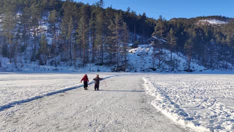 Niñas-Pequeñas-Caminando-Y-Tropezando-Juntas-En-Esquí-Y-Patines-De-Hielo---Jóvenes-Amigos-Felices-En-El-Lago-Congelado-Cubierto-De-Nieve