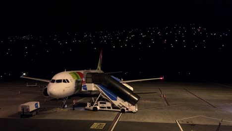 Toque-Las-Operaciones-Del-Aeropuerto-Durante-La-Noche,-Después-De-Aterrizar-El-Avión-En-La-Oscuridad,-Una-Escalera-Móvil-Del-Puente-De-Embarque-De-Pasajeros-Se-Mueve-Hacia-El-Avión-Para-Apoyar-La-Descarga-Segura-De-Pasajeros