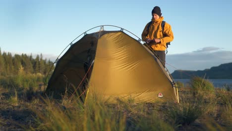 Junger-Entdecker-Steht-Bei-Starkem-Wind-Neben-Seinem-Zelt,-Umgeben-Von-Atemberaubender,-Unberührter-Skandinavischer-Natur-Während-Des-Sonnenuntergangs-In-Lappland,-Schweden