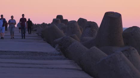 Menschen,-Die-Auf-Dem-Nordpier-Von-Karosta-Spazieren,-Bei-Romantischem,-Rot-Leuchtendem-Sonnenuntergang,-Mittlere-Aufnahme-Aus-Der-Ferne