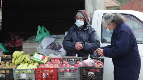 Una-Mujer-Vestida-Con-Ropa-De-Invierno-Y-Una-Máscara-Facial-Mercadería-Variedad-De-Frutas-En-Un-Puesto-En-Las-Aceras-En-Leiria,-Portugal