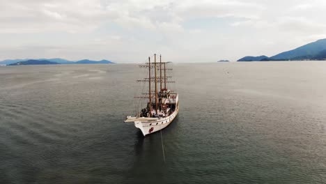 Grupo-De-Personas-En-Barco-Pirata-Navegando-En-El-Océano-De-Brasil-Durante-El-Día-Soleado,-Toma-Aérea-Hacia-Atrás