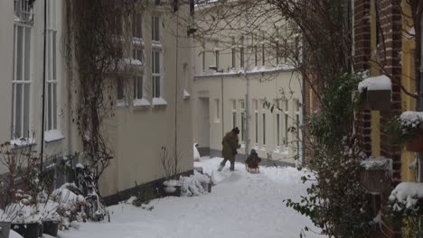 Escena-De-Nieve-En-Los-Países-Bajos-Con-Una-Familia-Joven-Cuyos-Niños-Montan-Un-Trineo-Que-Sus-Padres-Remolcan-En-Un-Pequeño-Callejón-Del-Centro-Histórico-De-La-Ciudad