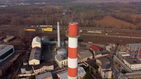 Vista-Aérea-De-Una-Chimenea-Industrial-Con-Un-Tren-En-El-Fondo,-Paso-Elevado