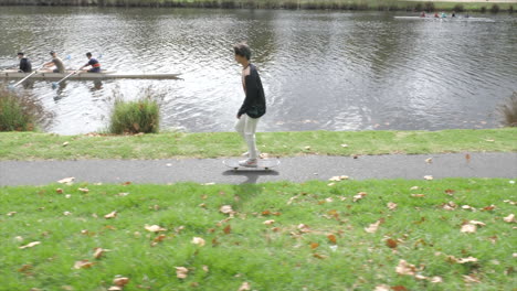 Skateboarder-Skates-Past-Rowers-On-River,-SLOW-MOTION