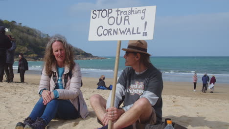 Two-Local-protesters,-a-male-and-female,-sit-on-the-beach-of-Carbis-Bay-Hotel,-St-Ives,-Cornwall