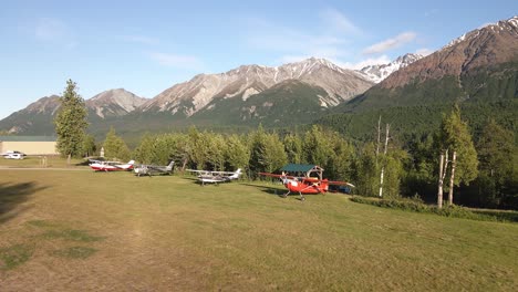 Imágenes-Aéreas-Girando-Alrededor-De-Aviones-Estacionados-A-Lo-Largo-De-Una-Pista-De-Aterrizaje-De-Hierba-En-La-Cordillera-Talkeetna-De-Alaska