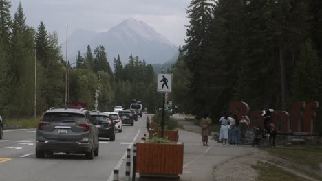 Tourist-getting-photographed-by-Banff-sign-with-busy-traffic-around