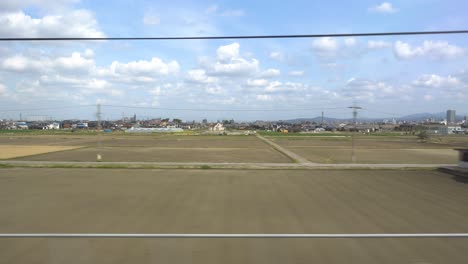 Wide-open-area-with-fields-and-beautiful-sky-passing-by-in-front-of-train-window