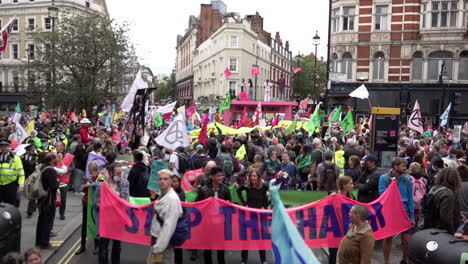 Hunderte-Von-Farbenfrohen-Extinction-Rebellion-Klimaschutzdemonstranten-Besetzen-Eine-Straßenkreuzung-In-Covent-Garden-Und-Stellen-Hinter-Einem-Rosa-Banner-Mit-Der-Aufschrift-„Stoppt-Den-Schaden“-Einen-Riesigen-Rosafarbenen-Tisch-Auf,-Der-Die-Straße-Blockiert.