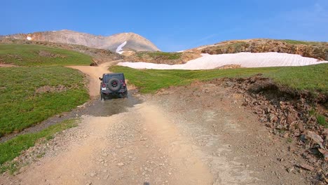 Punto-De-Vista-Siguiendo-Un-Vehículo-4wd-Que-Sube-Por-El-Sendero-Del-Paso-Del-Oso-Negro,-Pasando-Por-Colinas-Cubiertas-De-Hierba-Y-Ventisqueros-Sucios-En-Las-Montañas-De-San-Juan-Cerca-De-Telluride-Colorado