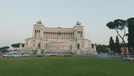 Panorámica-En-Cámara-Lenta-Del-Tráfico-De-Automóviles-En-La-Piazza-Venezia-O-La-Plaza-De-Venecia-Y-La-Luna-En-Roma-Al-Atardecer,-Italia