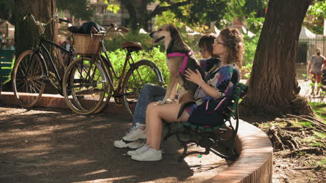 Szene-Mit-Frauen,-Die-Auf-Einer-Parkbank-Sitzen,-Eine-Mit-Einem-Hund-Auf-Dem-Schoß