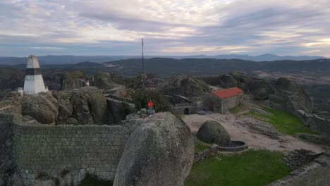 Woman-on-big-boulder-at-Monsanto-castle-during-sunrise,-Portugal