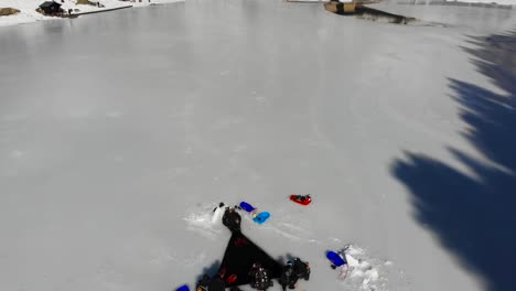 Aerial:-divers-entering-through-an-ice-hole-in-a-frozen-lake-and-pan-towards-a-church