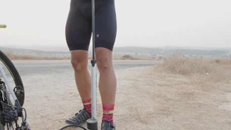 Manos-De-Un-Joven-Profesional-Arreglando-El-Neumático-De-Su-Bicicleta-Con-Una-Plomada-En-Medio-De-La-Carretera-Del-Desierto