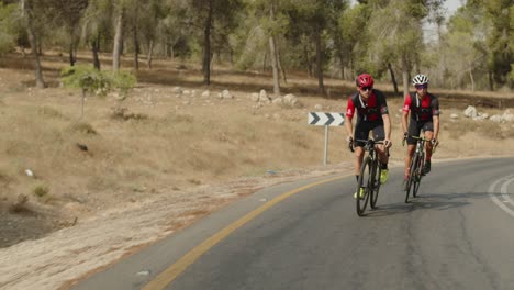 Zeitlupe-Zwei-Professionelle-Rennradfahrer,-Die-Auf-Der-Leeren-Straße-Des-Waldes-Fahren