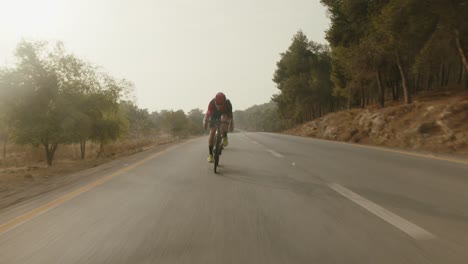 Zwei-Professionelle-Radfahrer-Fahren-In-Zeitlupe-Auf-Der-Leeren-Straße-Des-Waldes-Und-Die-Sonne-Strahlt-In-Die-Kamera