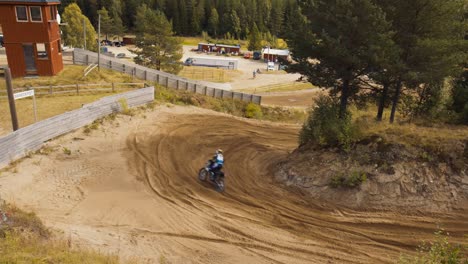 Una-Piloto-De-Motocross-Conduce-Cuesta-Abajo-Por-Una-Pista-De-Tierra,-Filmada-Desde-Arriba