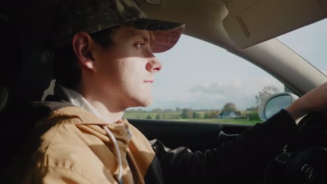 Young-Scandinavian-With-Sun-in-His-Face-Has-a-Discussion-on-Speaker-Phone-While-Driving-on-a-Countryside-Road---Handheld-Medium-Profile-Shot