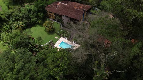 Revelación-Y-Panorámica-Lateral-Aérea-Que-Muestra-Un-Exuberante-Jardín-Tropical-Con-Piscina-En-La-Ladera-De-Una-Montaña-Con-Un-Pintoresco-Edificio-De-Hotel-De-Piedra