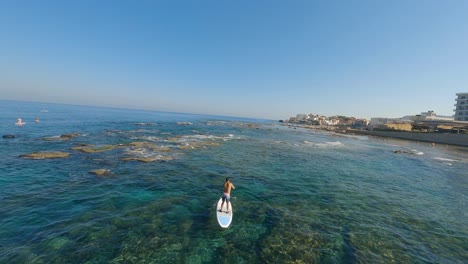 Fpv-drone-flying-through-group-of-young-people-paddle-surfing-on-a-sunny-beach-day