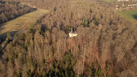 Kleine-Kapelle-Auf-Der-Spitze-Eines-Hügels,-Der-Von-Einem-Trockenen,-Braunen-Walddach-Bedeckt-Ist