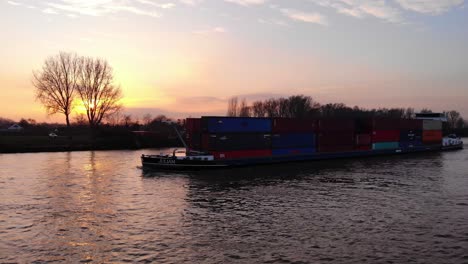 Aerial-View-Of-Stacked-Containers-On-Juliam-Cargo-Ship-Along-Oude-Maas-Against-Yellow-Sunset-Skies