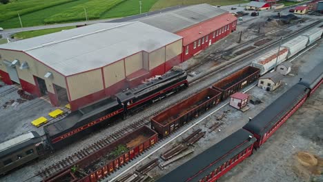 Una-Vista-Aérea-De-Un-Tren-De-Pasajeros-De-Vapor-Antiguo-Que-Se-Acerca-A-La-Estación-A-Través-Del-Patio-De-Carga