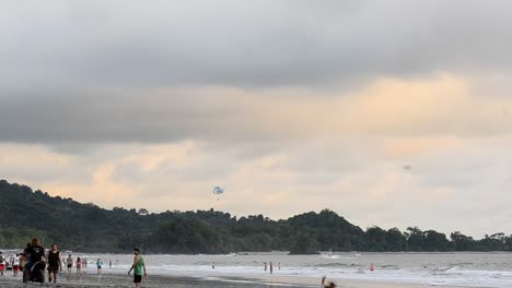 Playa-Llena-De-Gente-Durante-La-Puesta-De-Sol-Con-Un-Hombre-En-Una-Motocicleta-Conduciendo-Por