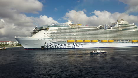 Drone-shot-of-the-Wonder-Of-The-Seas-Royal-Caribbean-cruise-ship-docked,-wide-rotating-with-small-boat-in-the-foreground