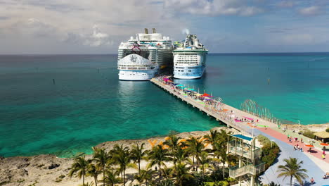 Wide-aerial-shot-of-CoCoCay-island-with-water-slides-flying-towards-a-Royal-Caribbean-cruise-ship-in-the-background,-Wonder-Of-The-Seas