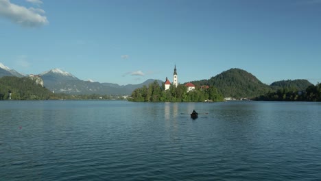 Paar-Rudert-Romantisch-Im-Pletna-Boot-Zur-Verträumten-Insel-Bled-Am-See,-Luftaufnahmen