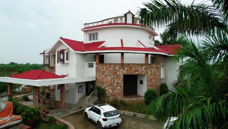 View-to-the-side,-aerial-with-drone,-of-a-vacation-house-in-Vadodara,-India,-three-floors-with-Hindu-statue-decoration,-surrounded-by-forests,-clearing-and-relaxing-sky-to-meditate-and-rest