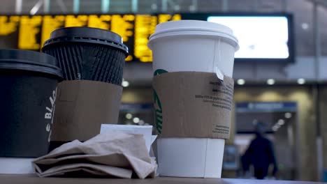 Gruppe-Von-Entsorgungsbechern-Auf-Dem-Tisch-Im-Bahnhof-Kings-Cross-Mit-Bokeh-Hintergrund-Von-Vorbeigehenden-Menschen