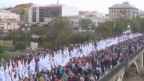 Penitents-march-during-a-procession-crossing-the-Triana-bridge-in-celebration-of-the-Holy-Week-in-Seville,-Spain