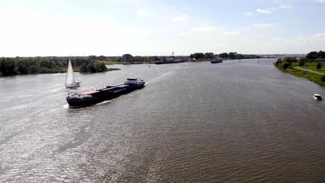 Antena-Sobre-Oude-Maas-Con-Carguero-Draga-Pasando-Por-Un-Velero-En-Un-Día-Soleado