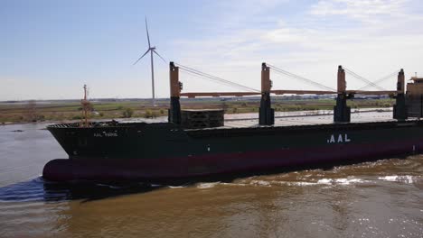 Vista-Lateral-Del-Puerto-Aéreo-Del-Buque-De-Carga-Aal-Paris-Que-Viaja-A-Lo-Largo-De-Oude-Maas-Con-Una-Turbina-Eólica-En-Segundo-Plano